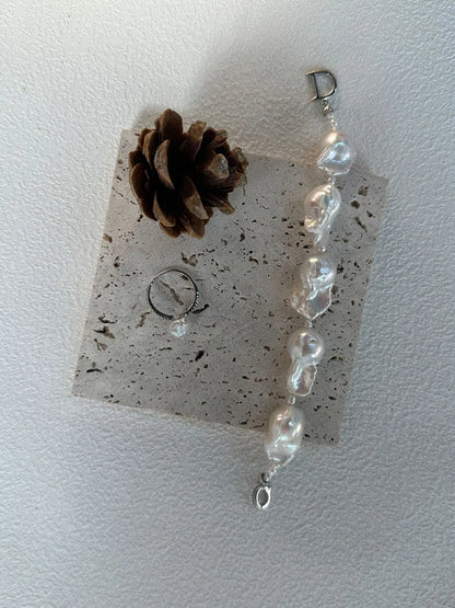 Vertical flatlay of the rice and large baroque pearl strand with a pearl ring on travertine slab.