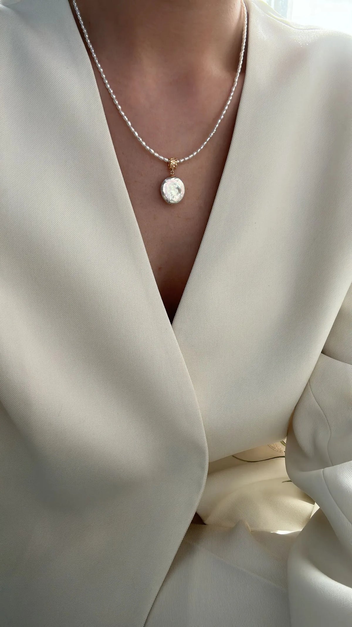 Close-up of model showcasing the Roman coin pearl pendant resting on the collarbone.