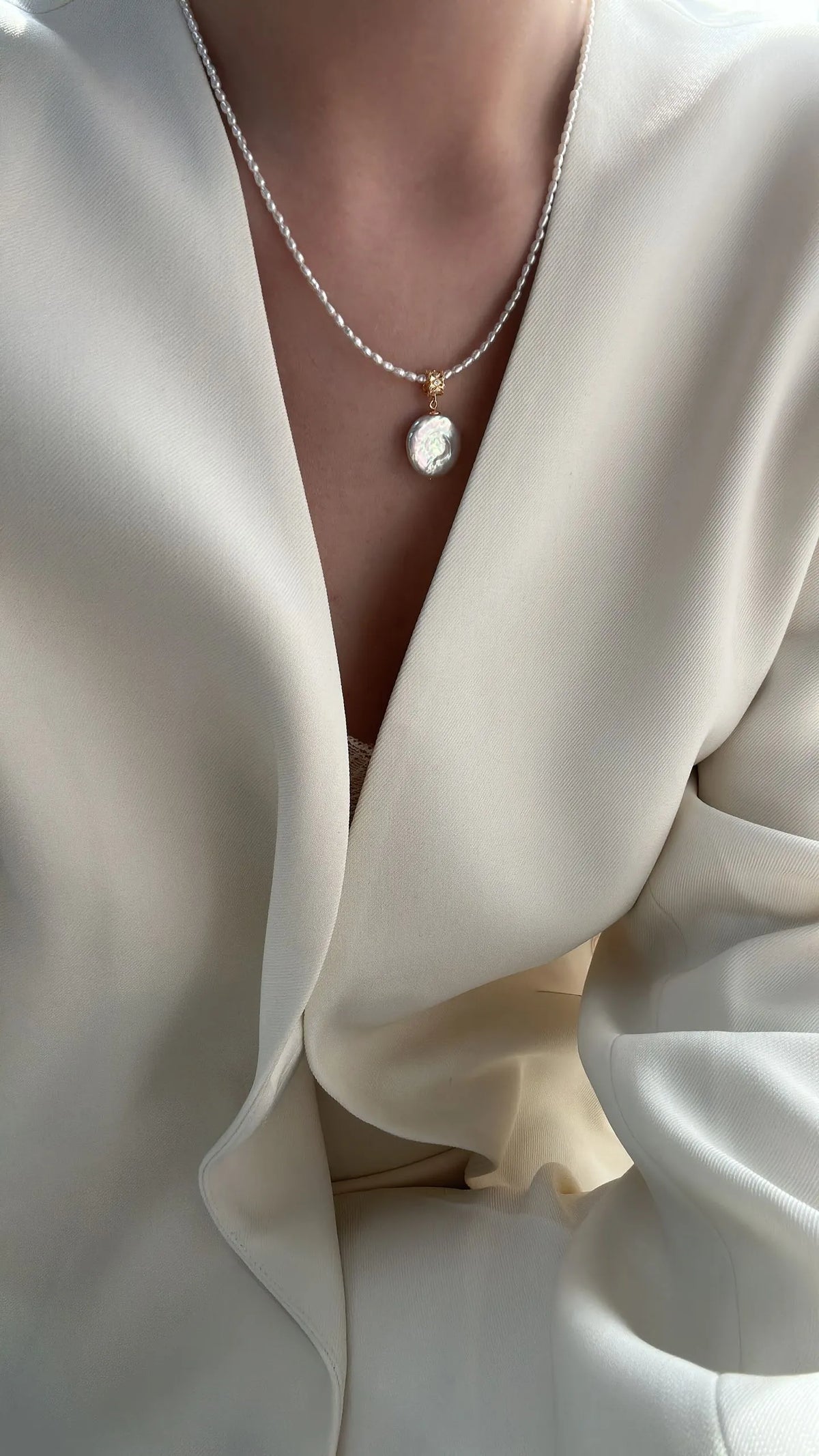 Model wearing the Roman coin pearl pendant necklace with a white deep V-neck blazer
