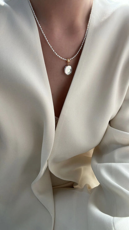 Model wearing the Roman coin pearl pendant necklace with a white deep V-neck blazer