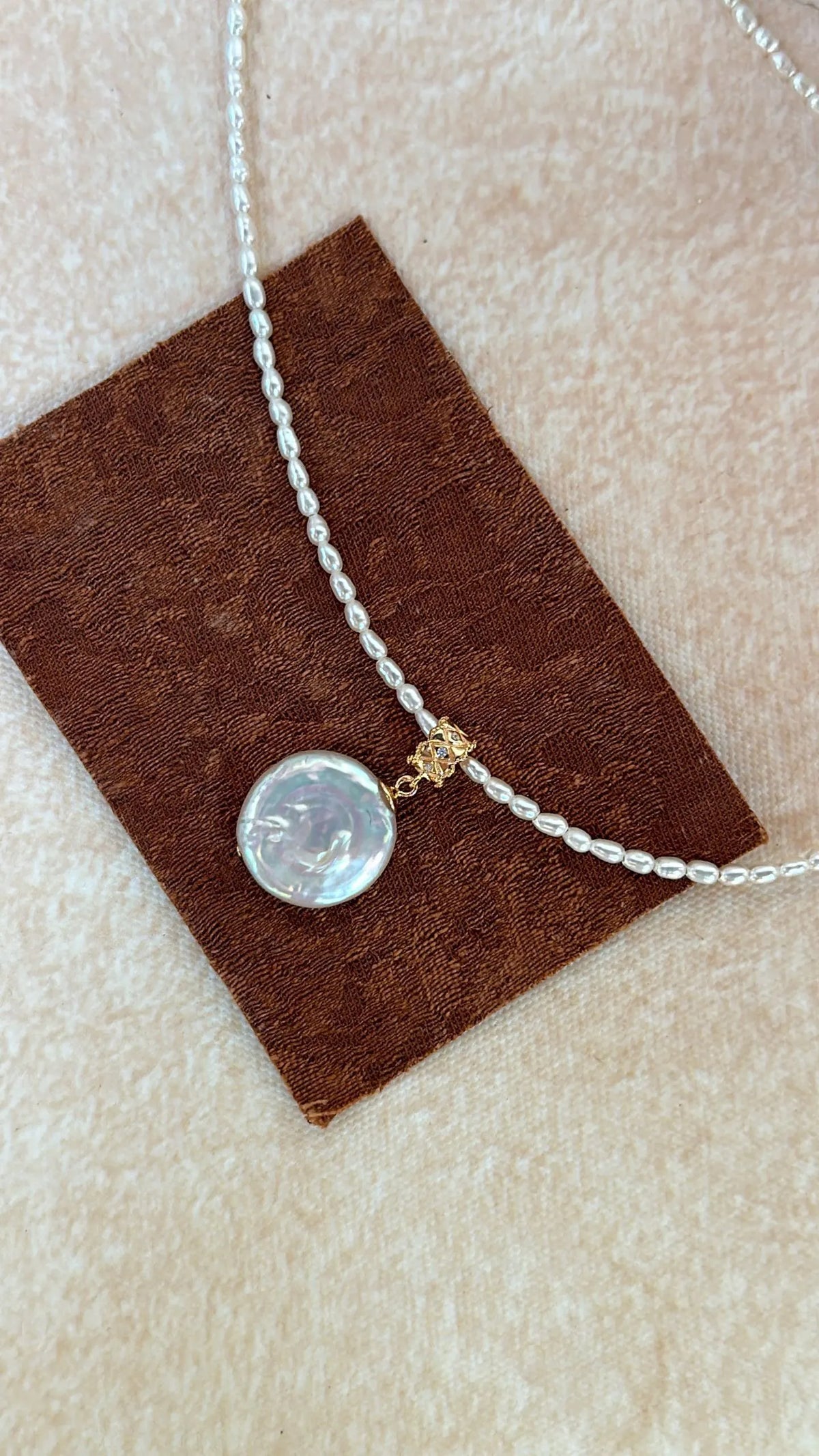 Close-up flatlay of the Roman coin pearl pendant on brown leather.