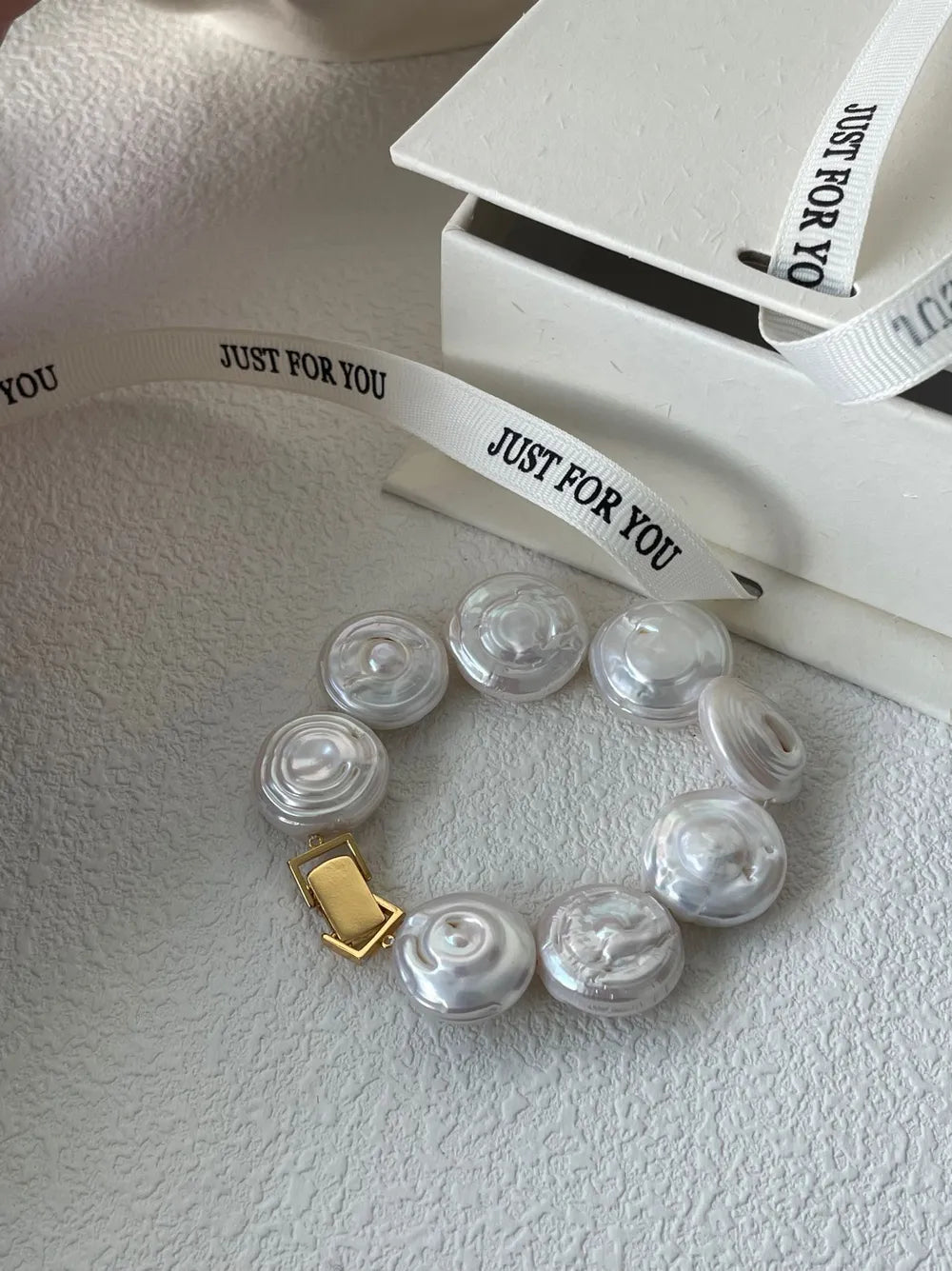 Roman Holiday coin baroque pearl bracelet displayed beside a white gift box and printed ribbon.