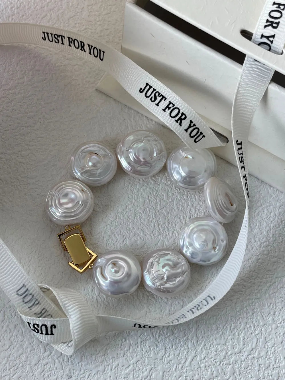 Flat button coin baroque pearl bracelet arranged on white background with custom ribbon prop.