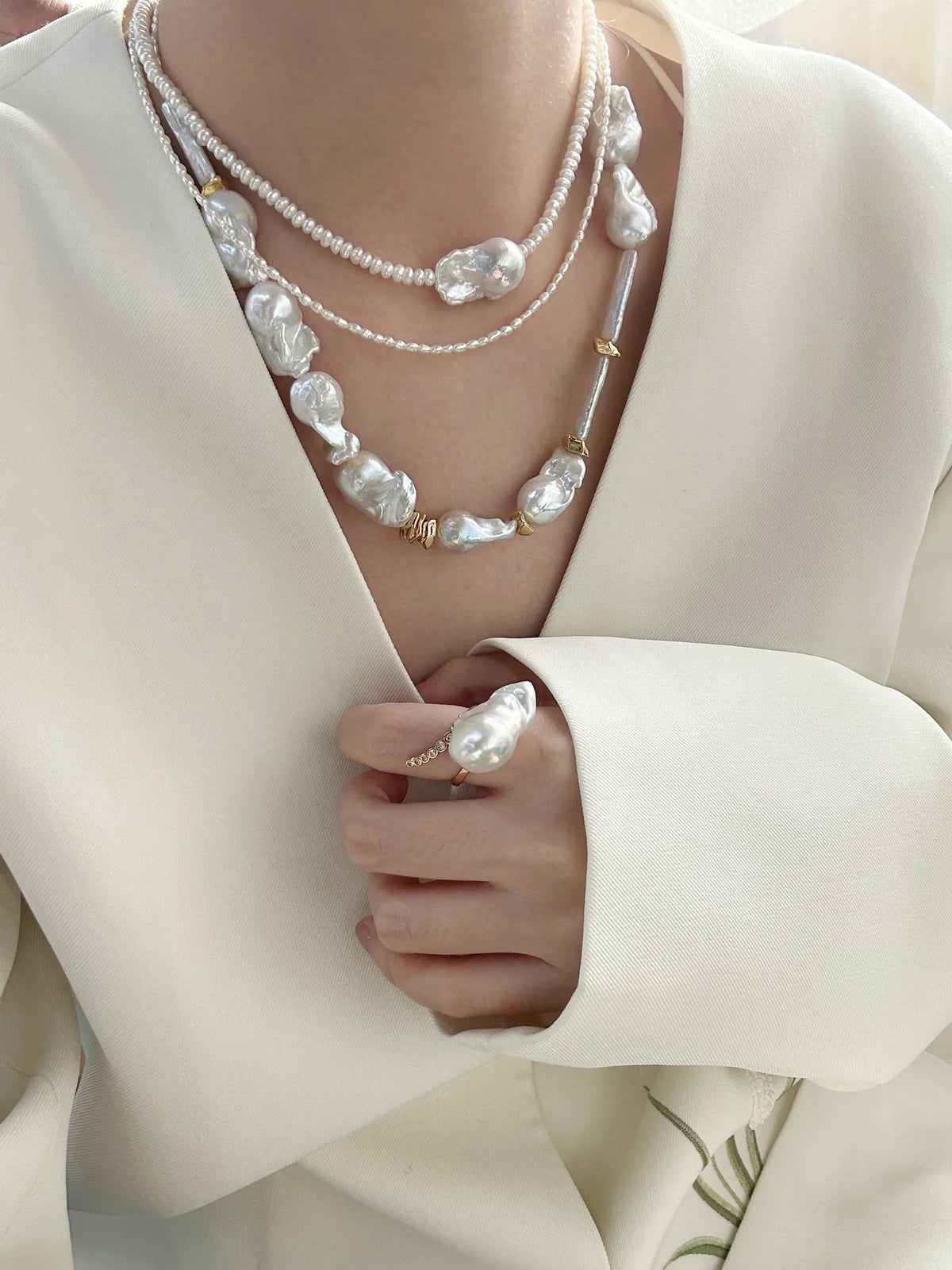 Statement barn-style baroque pearl necklace stack worn with a low-cut white suit jacket.