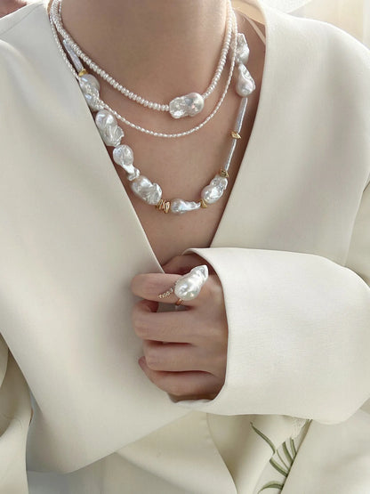 Statement barn-style baroque pearl necklace stack worn with a low-cut white suit jacket.