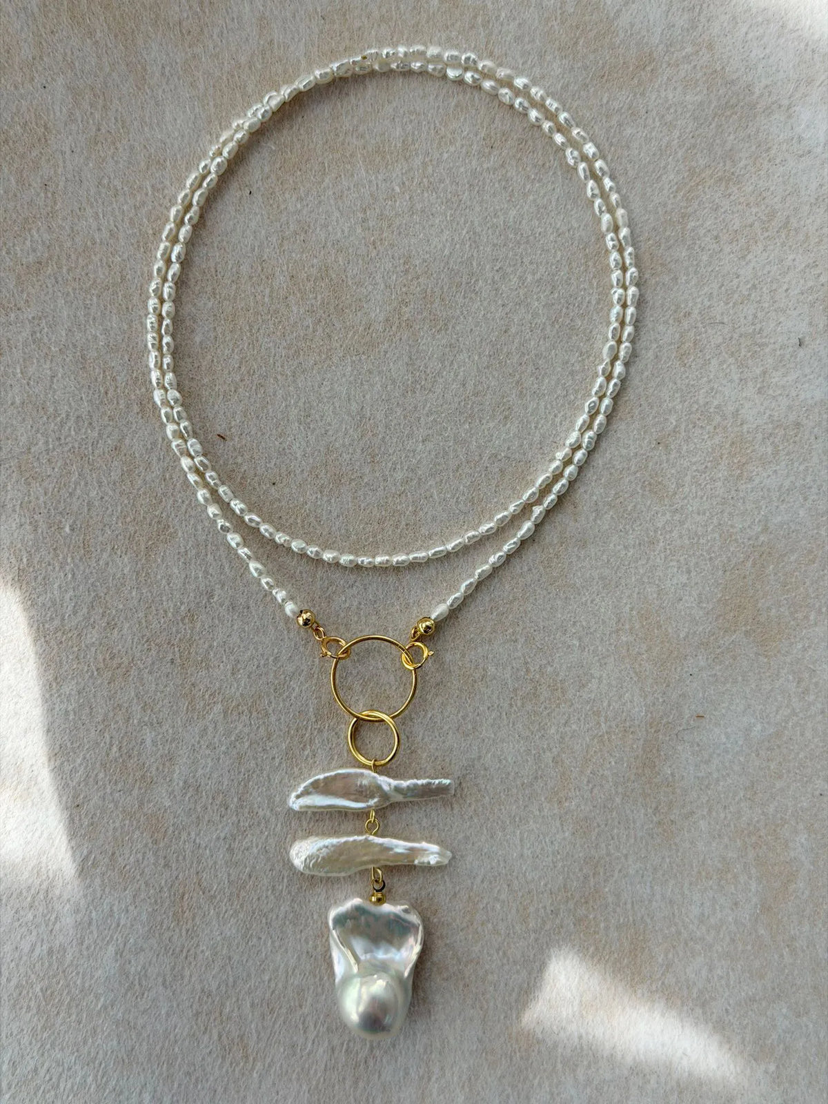 Gold-plated S925 sterling silver geometric ring baroque pearl necklace on soft textured background.