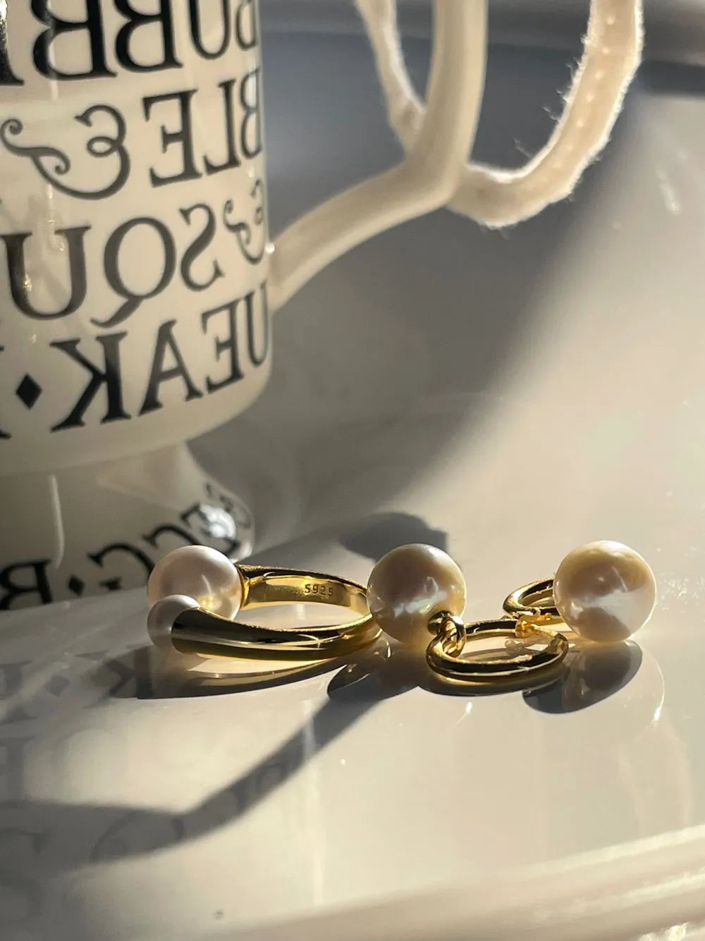Close-up view of the crystal baroque pearl huggie earrings showing S925 hallmark stamp under sunlight.
