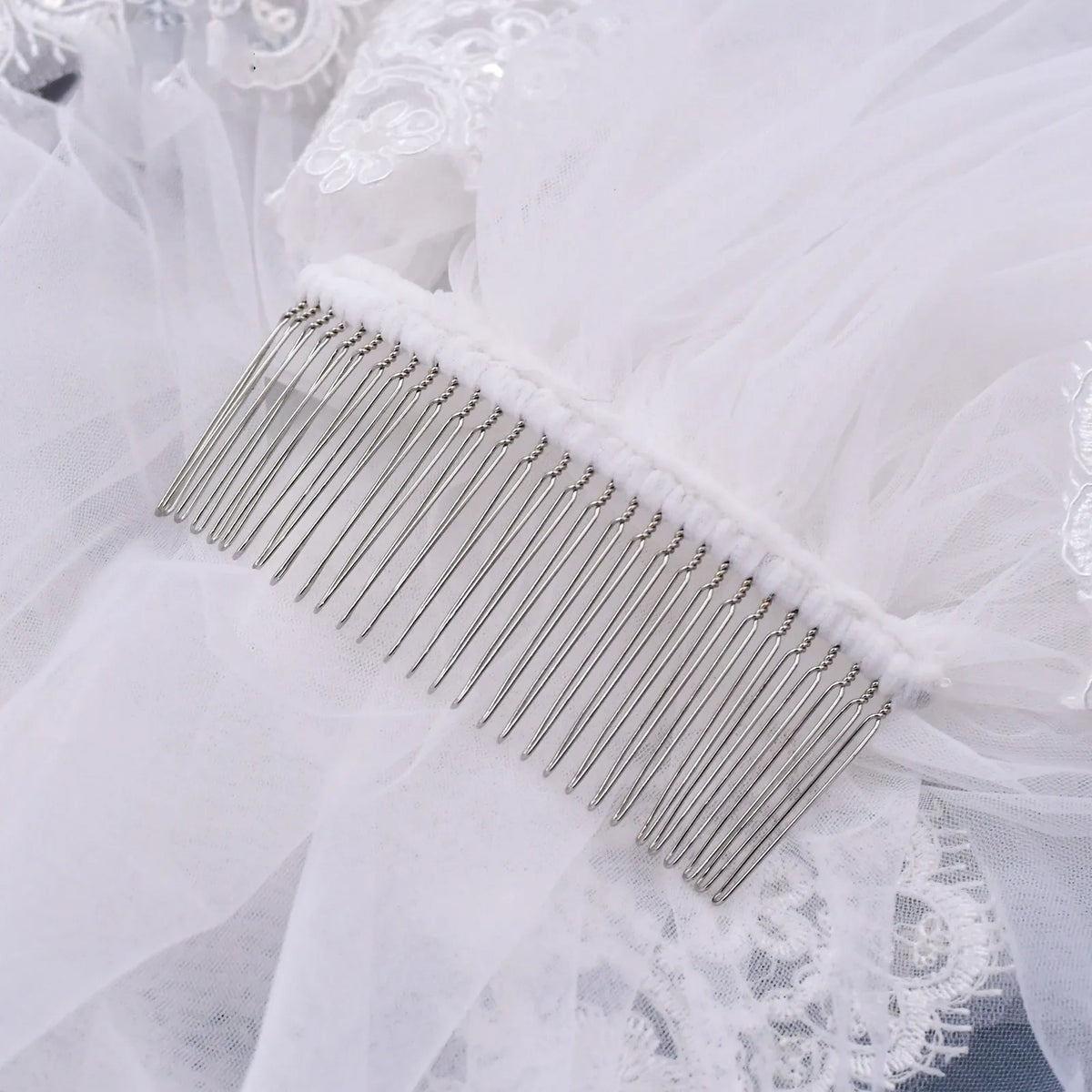 Close-up of sturdy metal hair comb stitched onto gathered sheer ivory tulle mesh