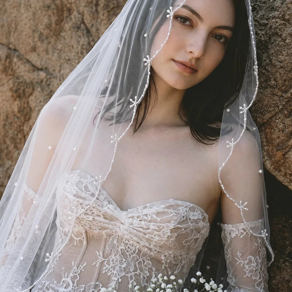 Close-up portrait of bride framed by soft tulle veil showing delicate bead floral branch details and scattered pearls