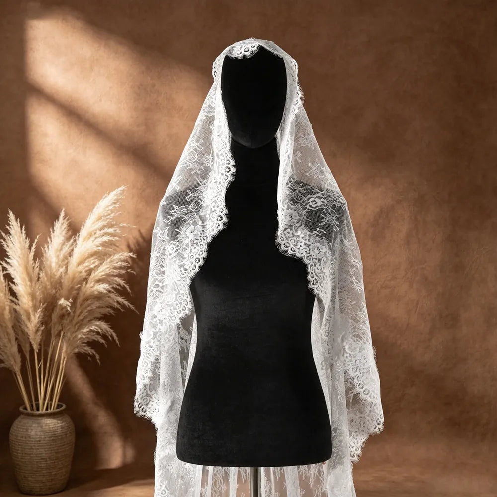 Close-up shot of bride with closed eyes behind the sheer white mantilla veil, showing the high-transparency mesh and romantic facial framing lace