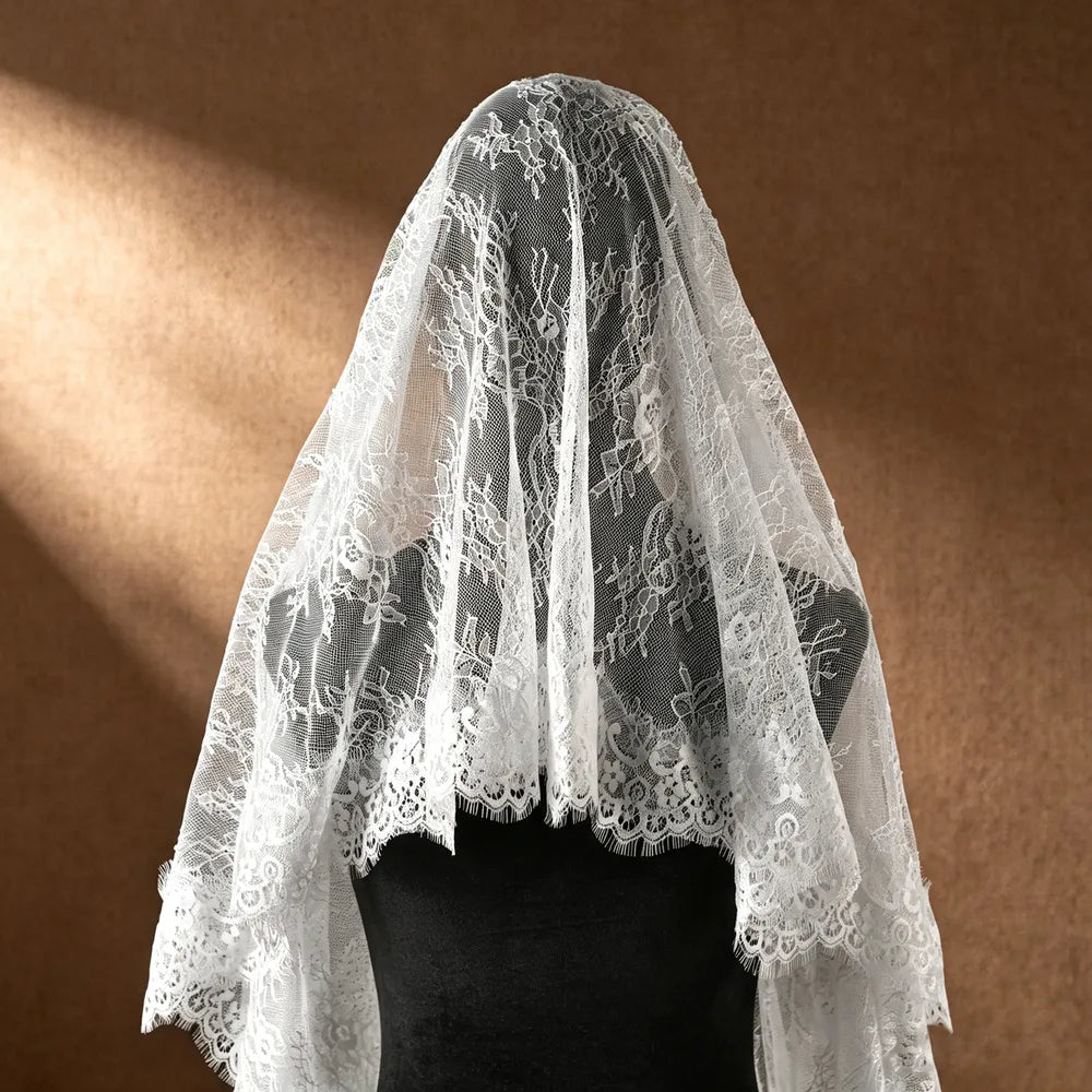 Close-up shot of bride with closed eyes behind the sheer white mantilla veil, showing the high-transparency mesh and romantic facial framing lace
