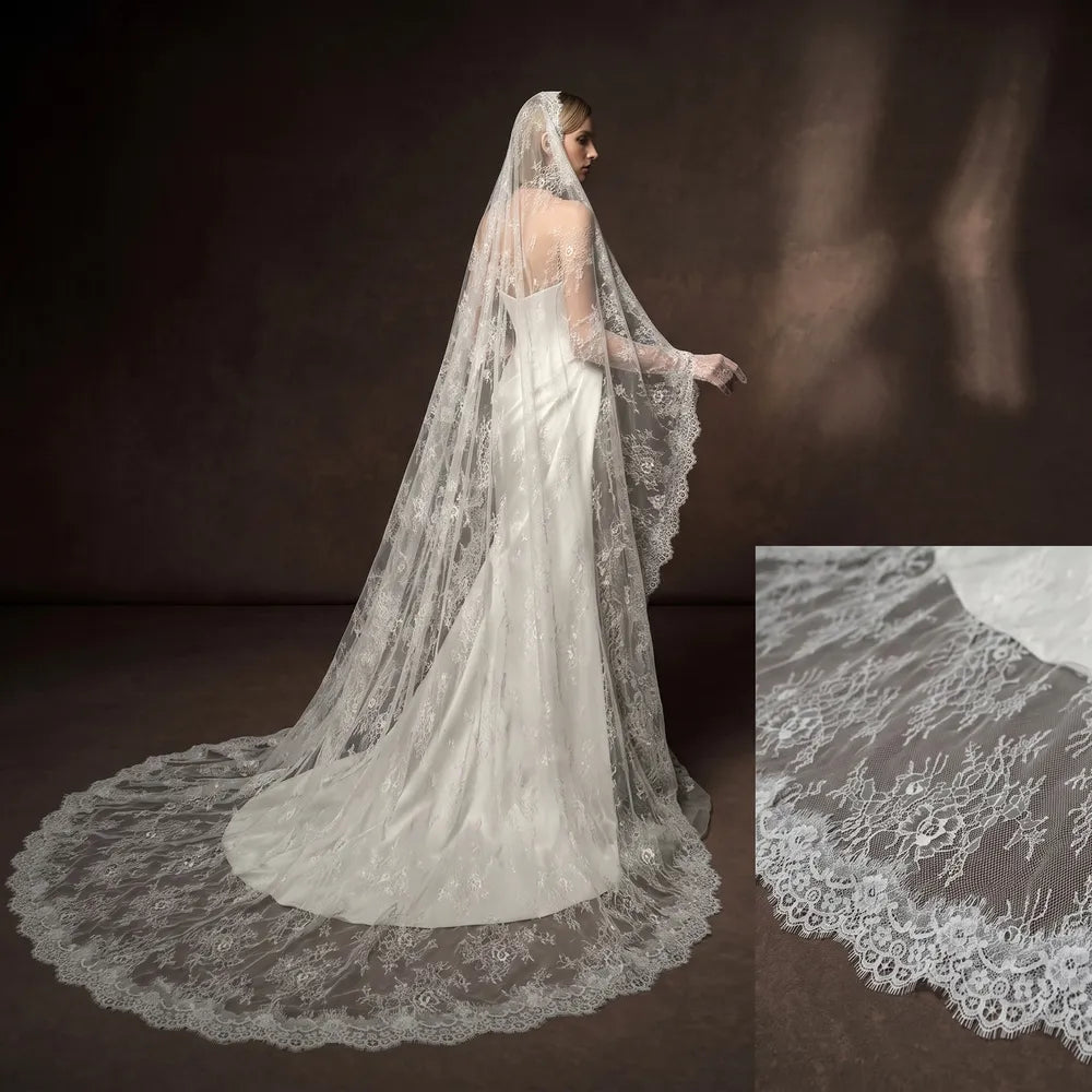 Bride in pleated strapless bridal dress sitting on a vintage wooden armchair, draped softly in a sheer white lace mantilla veil