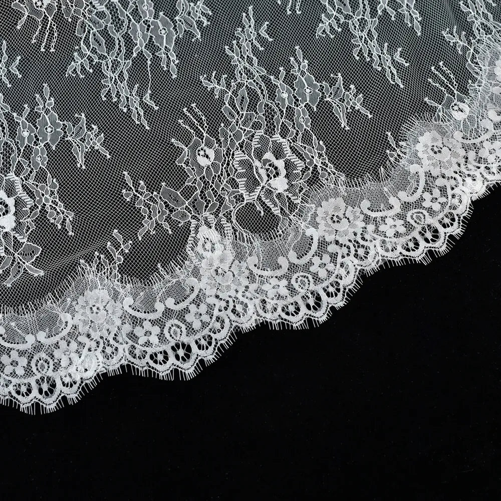Macro photography close-up showing delicate botanical embroidery patterns and sheer netting on the mantilla bridal veil fabric