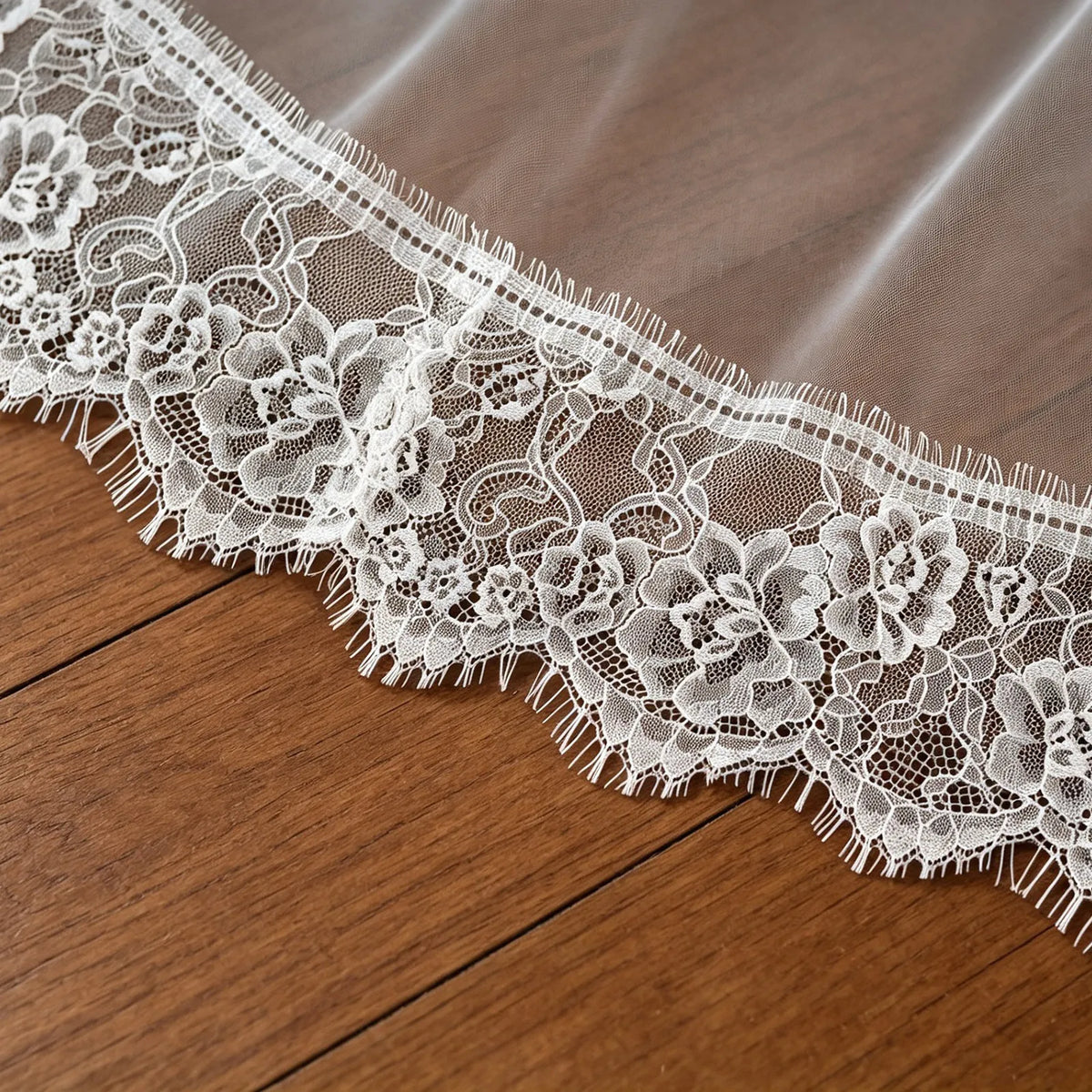 Extreme close-up shot highlighting the intricate floral embroidery and Chantilly eyelash lace scalloped trim along the bottom hem laid on a wooden surface