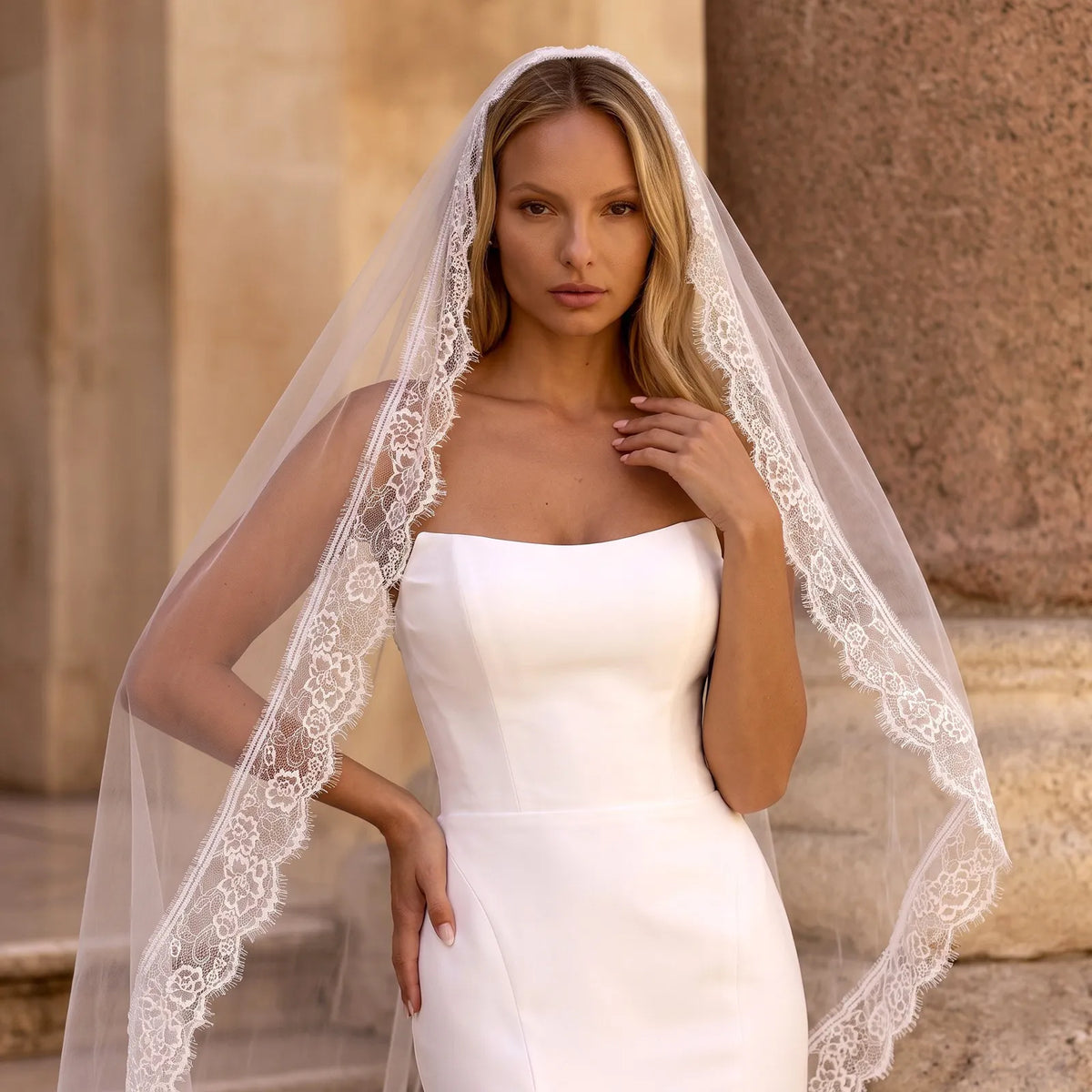 Close-up side profile of the veil on a mannequin showing soft white tulle folds alongside rich floral eyelash lace edging against a warm textured backdrop