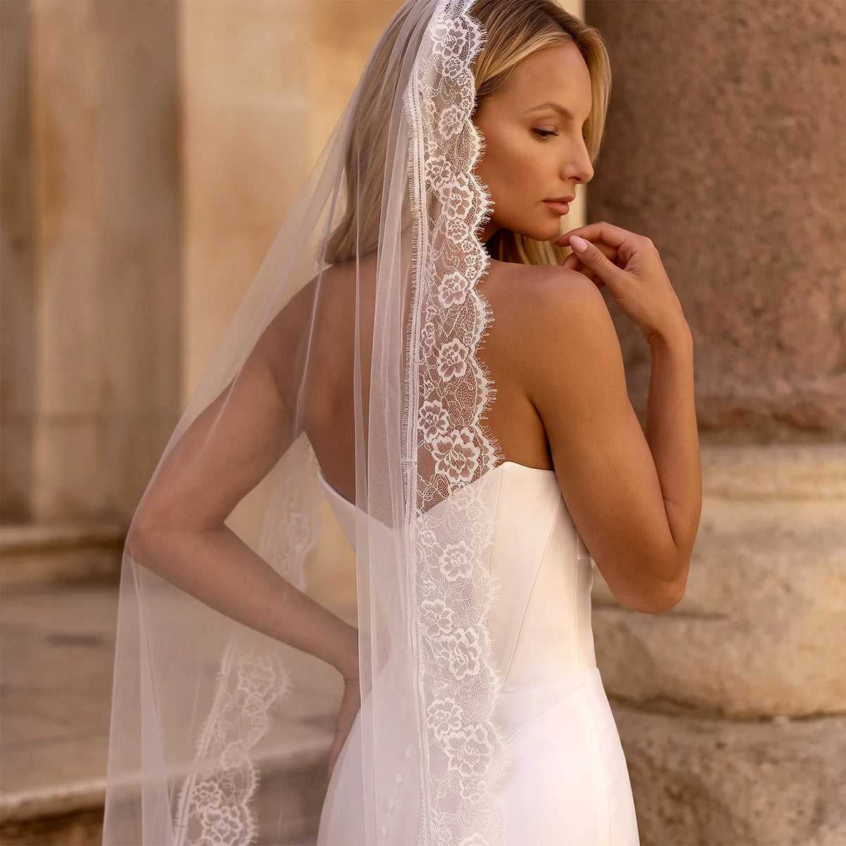 Over-the-shoulder portrait of bride in a strapless gown displaying the elegant drape of sheer tulle and scalloped lace trim across her upper back