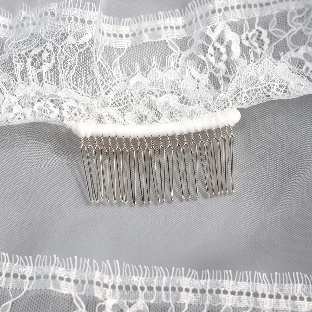 Macro photography close-up showing the silver metal hair comb wrapped in white ribbon and securely stitched to the lace gathering of the bridal veil