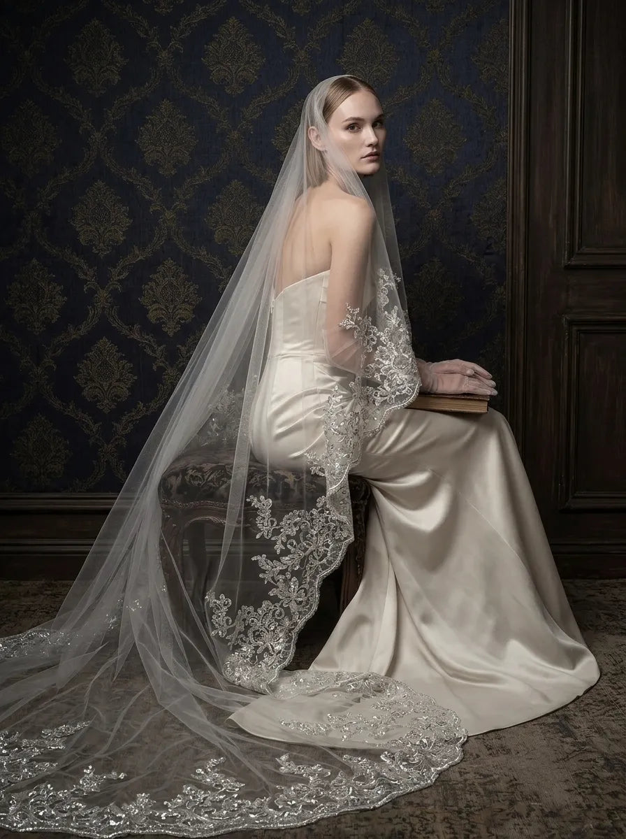 Bride seated wearing single-tier cathedral veil with blusher and sequin lace border cascading over satin dress