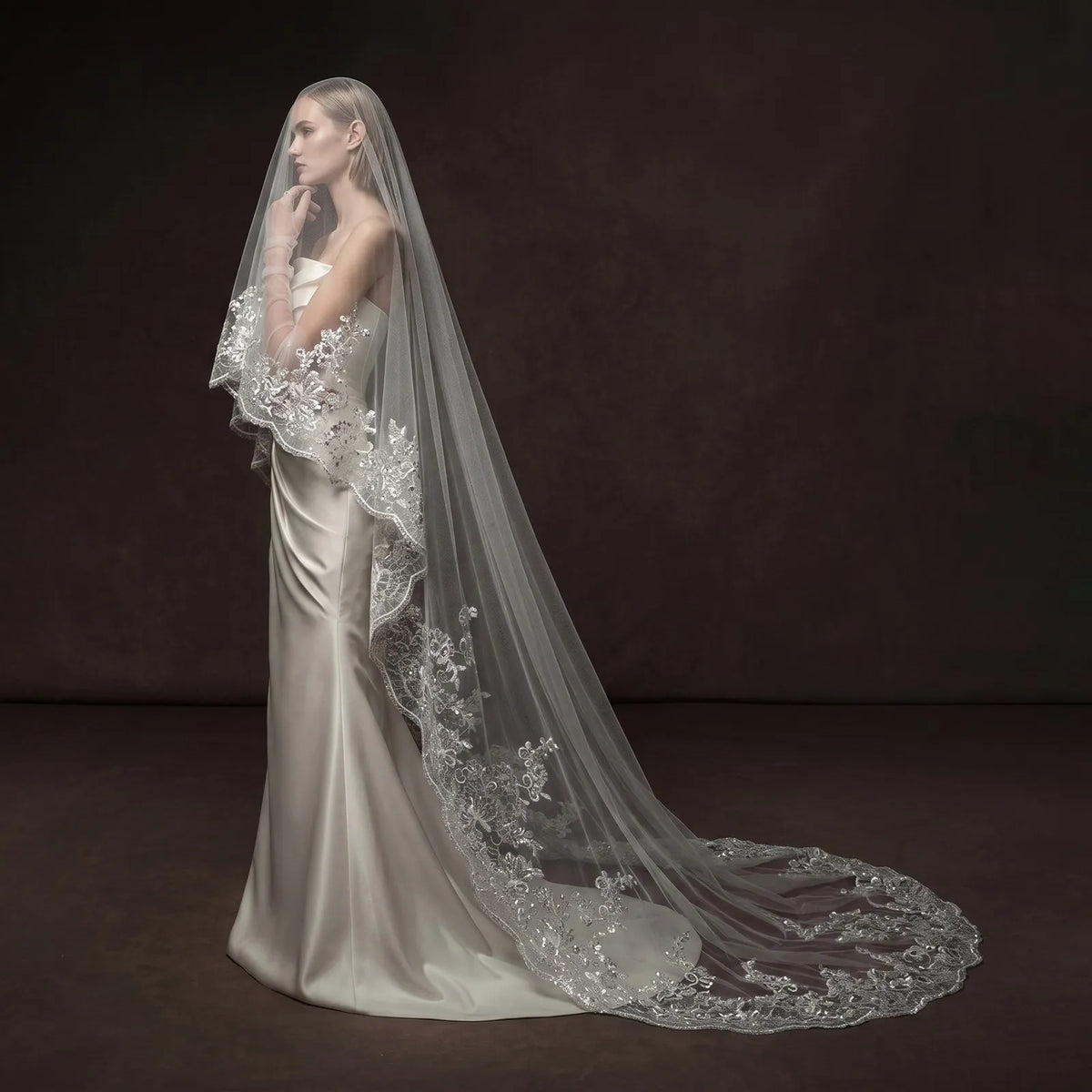 Full length side profile of bride in satin gown with sheer single-tier cathedral veil forming a long sweeping train