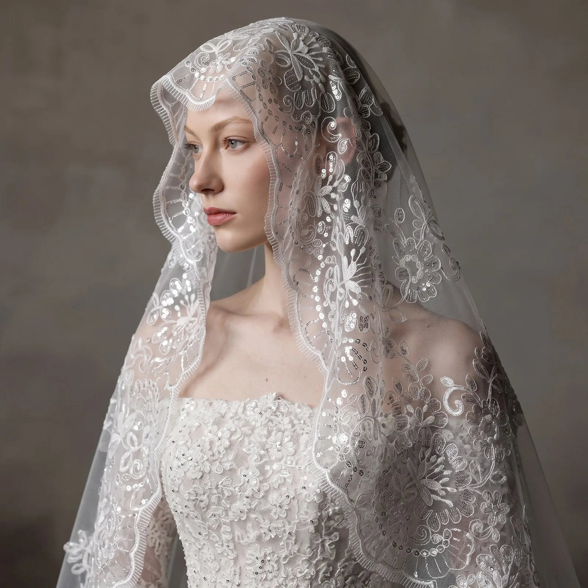 Close-up portrait of bride with cathedral veil draped softly around face, highlighting shiny clear sequins on lace