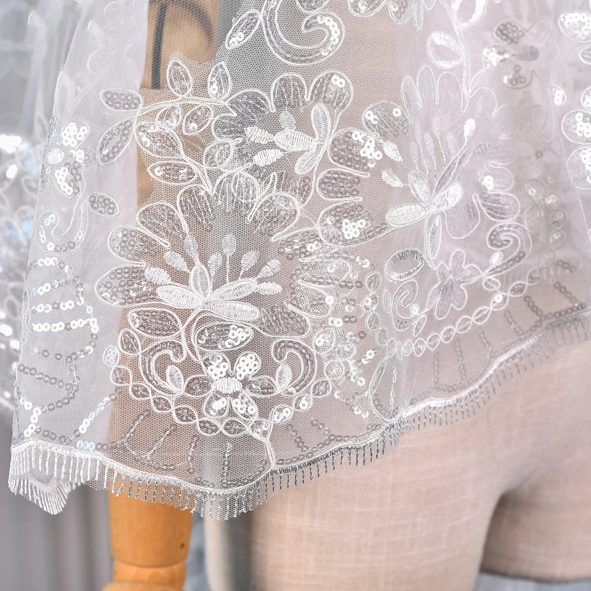 Extreme close-up shot of detailed flower lace applique embroidered with silver sequins and eyelash fringe trim
