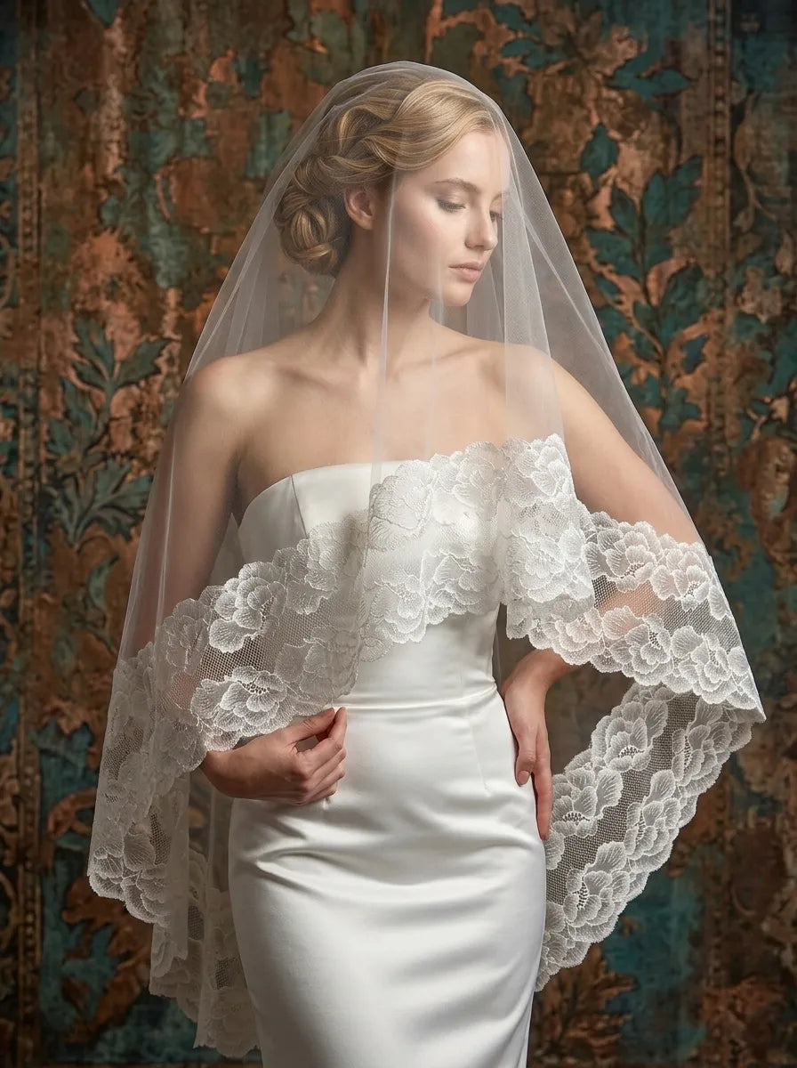 Side profile of blonde bride wearing sheer blusher veil with wide floral lace edge over strapless satin dress