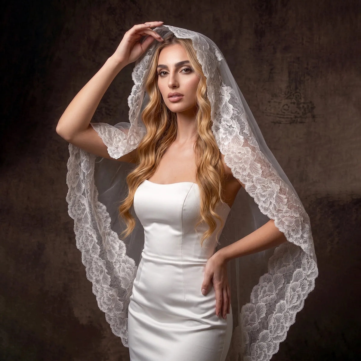 Fashion bridal portrait holding wide lace veil edge as a romantic hood over blonde wavy hair
