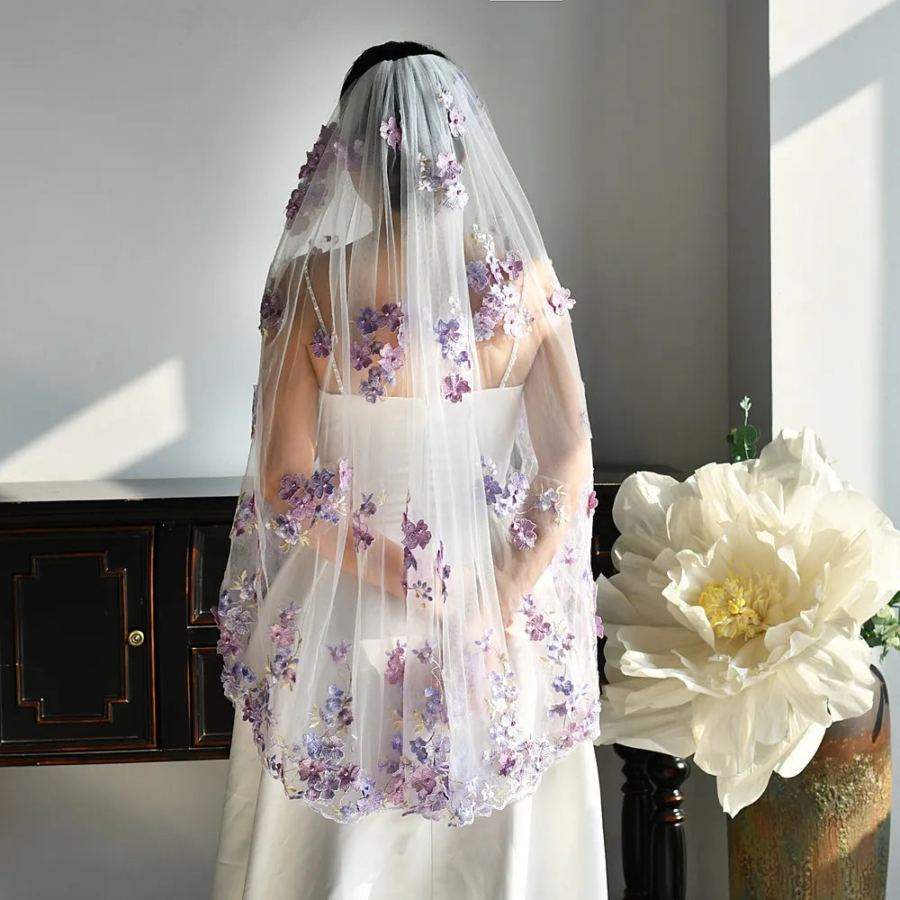 Macro photography close-up highlighting 3D lavender, lilac, and purple embroidered flower appliques with hand-set central pearls on soft white bridal tulle fabric