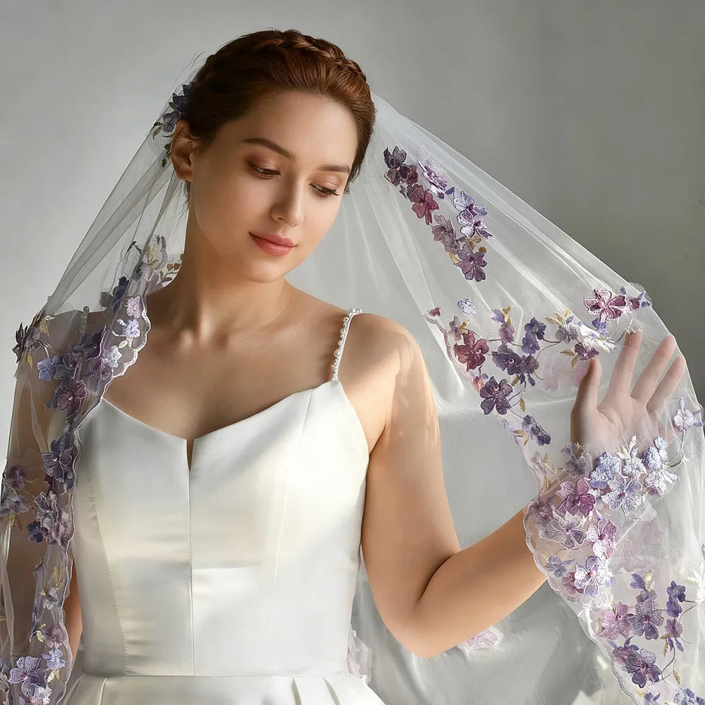 Half-length view of bride with elegant braided up-do softly lifting the scalloped purple botanical lace trim to show fine thread embroidery and pearl embellishments
