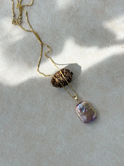 Iridescent square baroque pearl necklace flatlay with pinecone under natural sunlight.