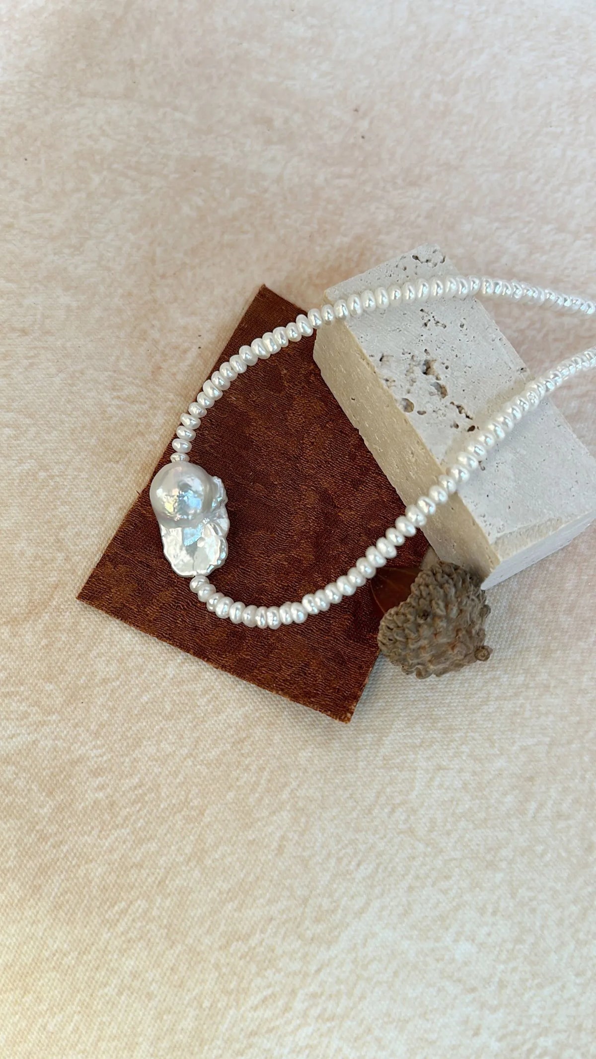 Statement organic baroque pearl choker displayed on a stone texture block