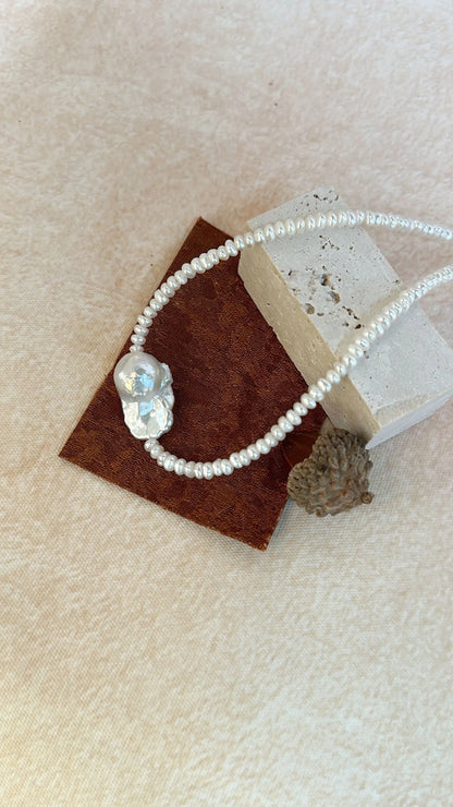 Statement organic baroque pearl choker displayed on a stone texture block