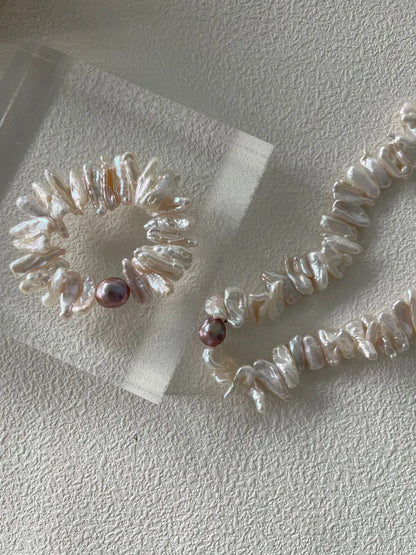 Hand stretching a stick baroque pearl bracelet displayed next to a long matching pearl necklace.