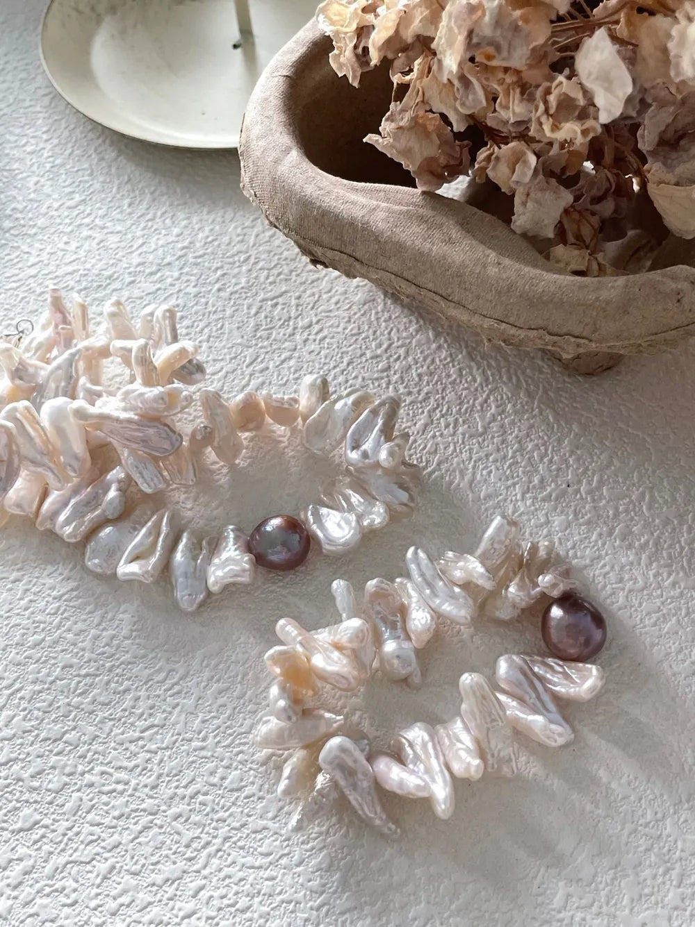 Stick baroque pearl elastic bracelet and strand necklace on white textured surface.
