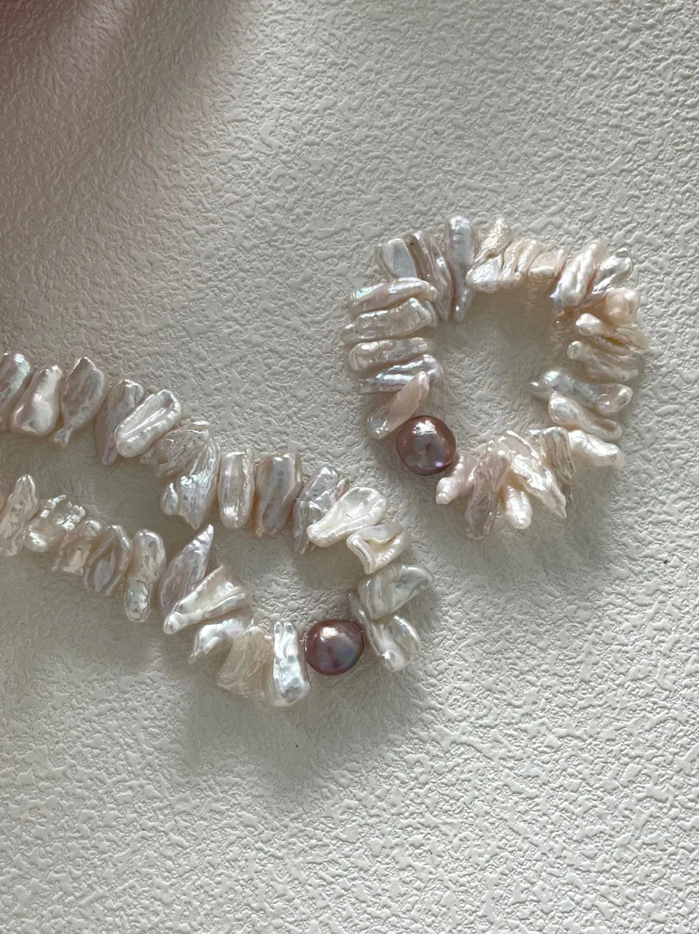 Two stick baroque pearl elastic bracelets with purple main pearls displayed near a dried floral bowl.