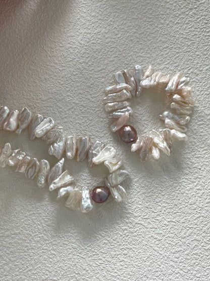 Two stick baroque pearl elastic bracelets with purple main pearls displayed near a dried floral bowl.