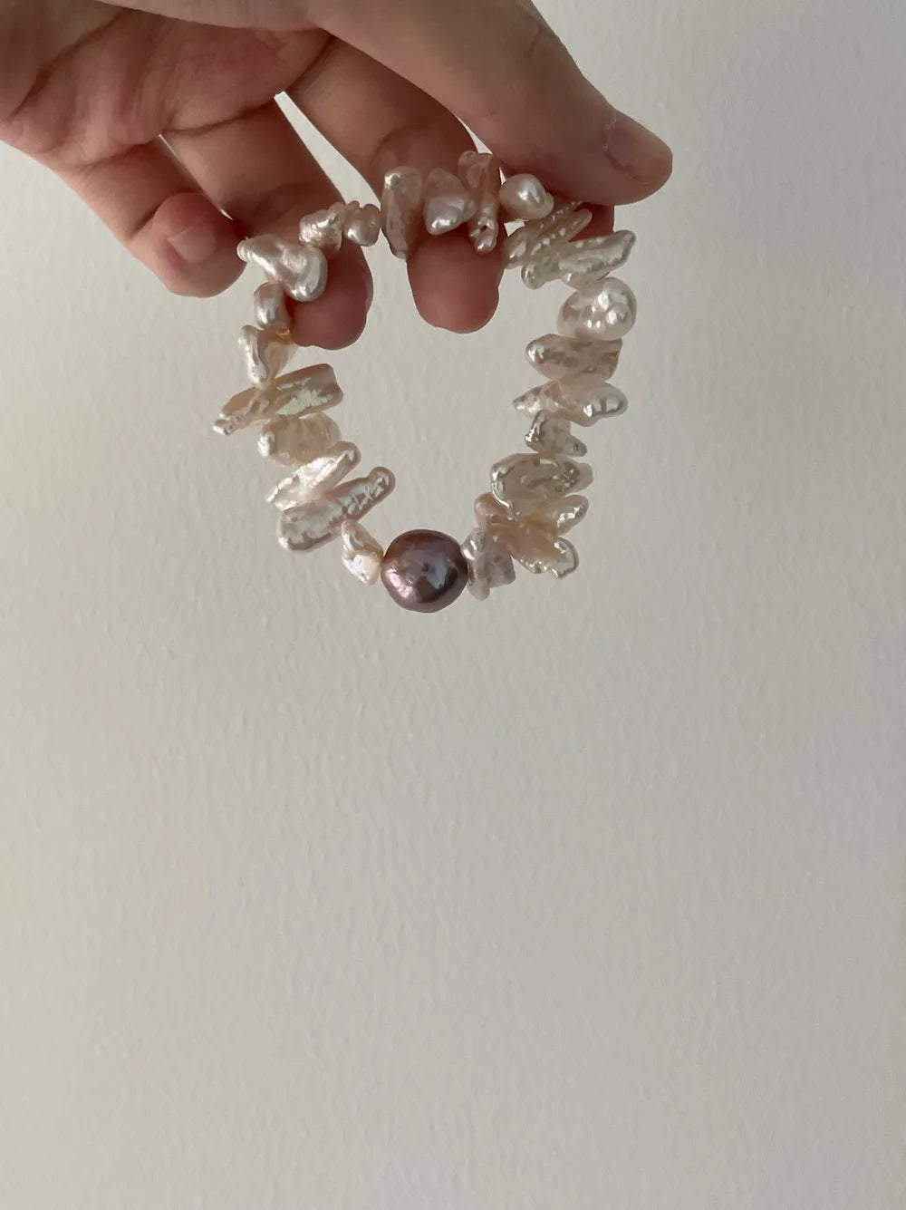 Hand holding the stick baroque freshwater pearl elastic bracelet with a central purple pearl accent.