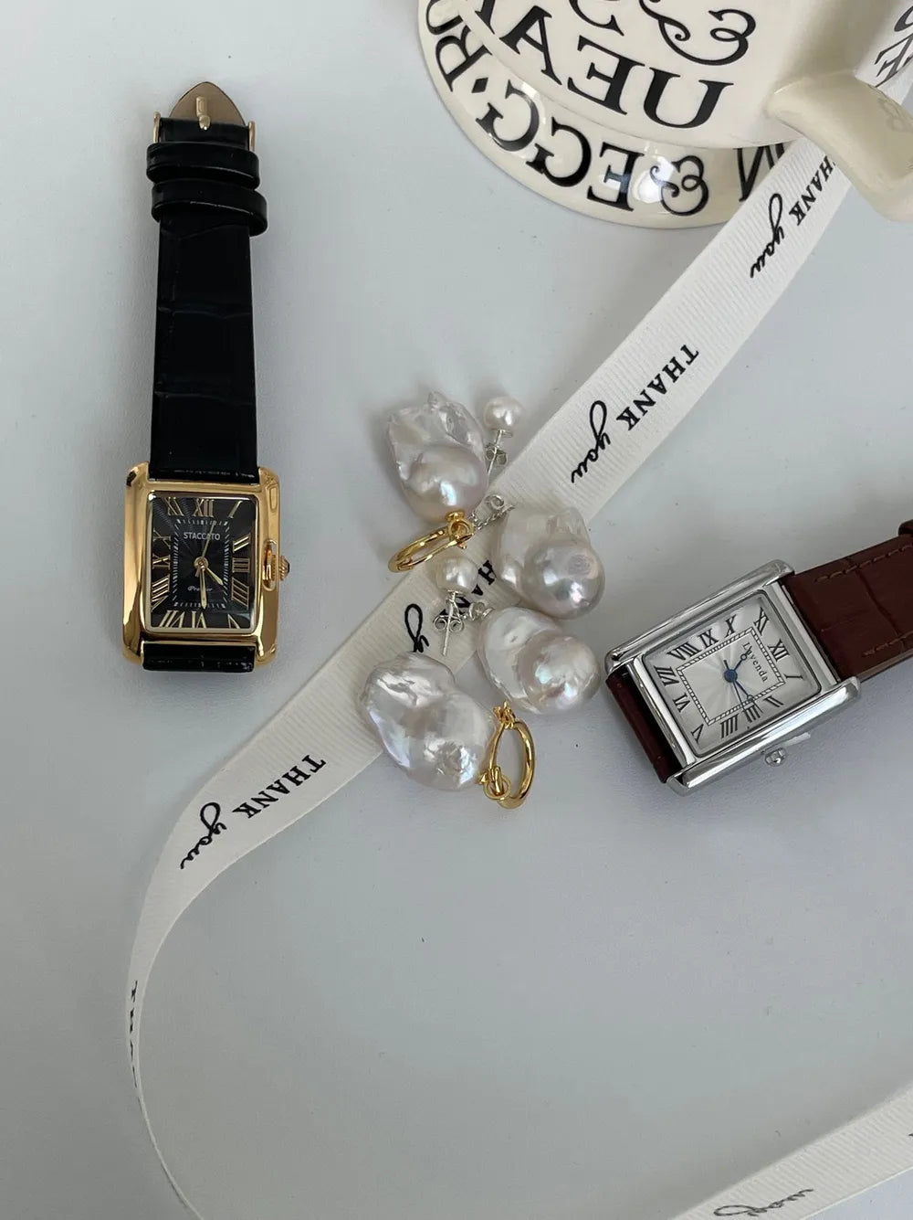 Flame-tailed baroque pearl huggie earrings paired with a black leather watch.