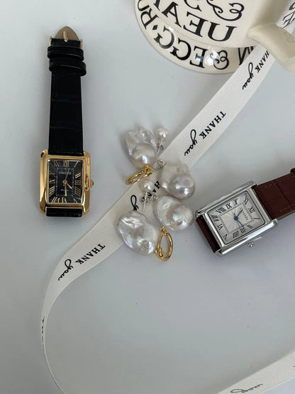 Flame-tailed baroque pearl huggie earrings paired with a black leather watch.