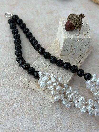 Angled view showcasing the luster and multi-dimensional texture of clustered baroque pearls on a black onyx chain.