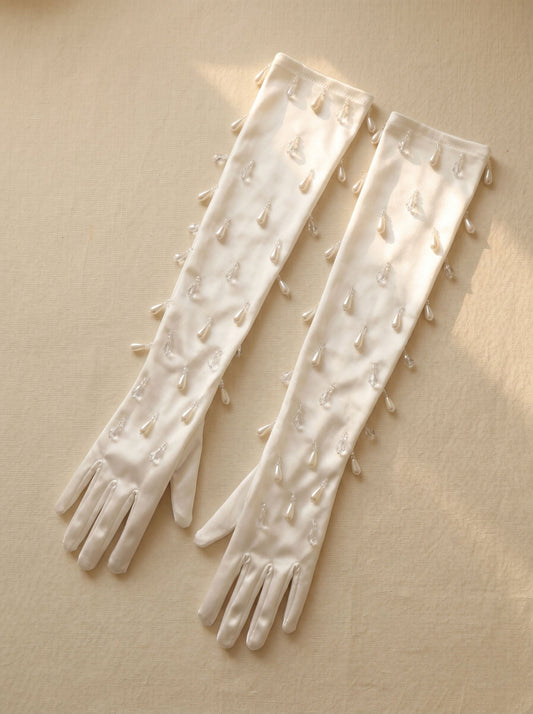 Elegant close-up of 50-55cm opera length white stretch satin bridal gloves adorned with cascading high-refraction glass teardrop charms and ruched wrist detailing.