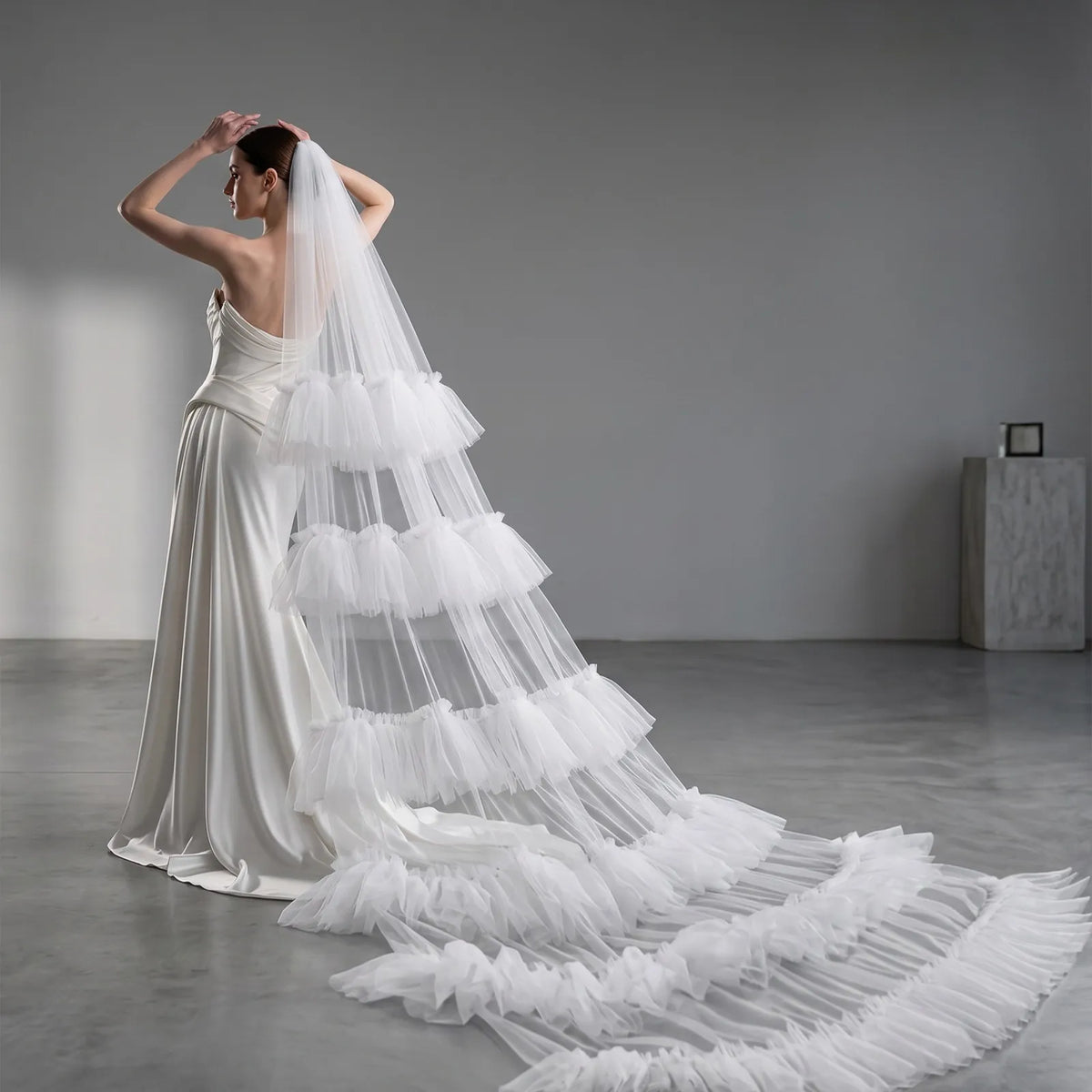 Side profile shot of bride in strapless dress showing flowing tiered ruffle tulle veil trailing on concrete floor