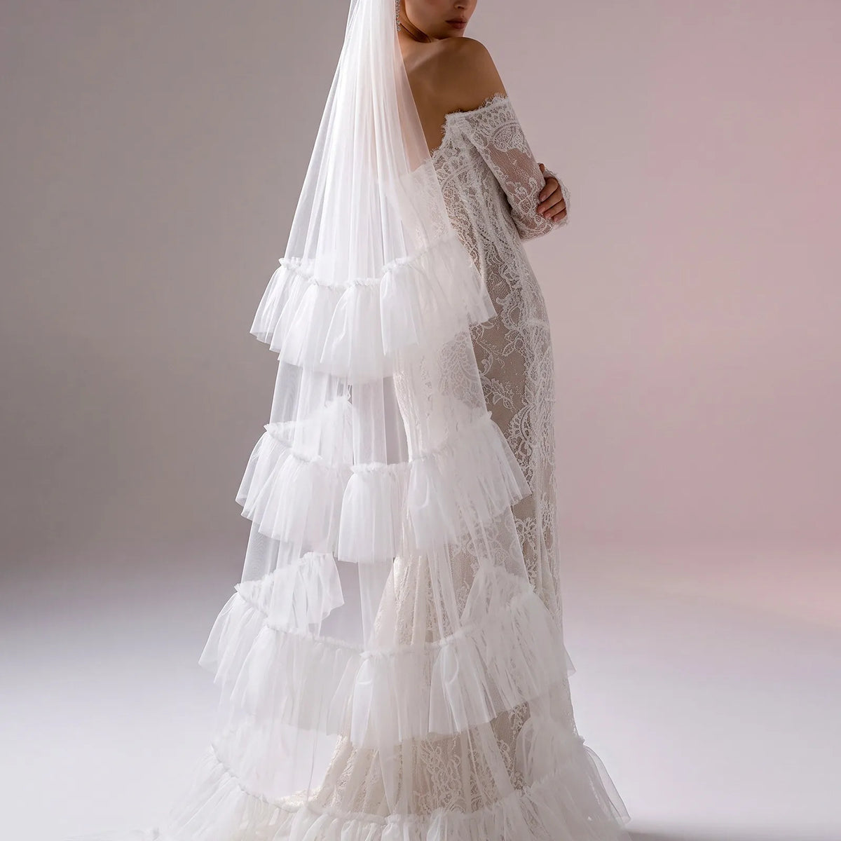 Three-quarter side view of bride wearing lace wedding dress with cascading tiered ruffle veil