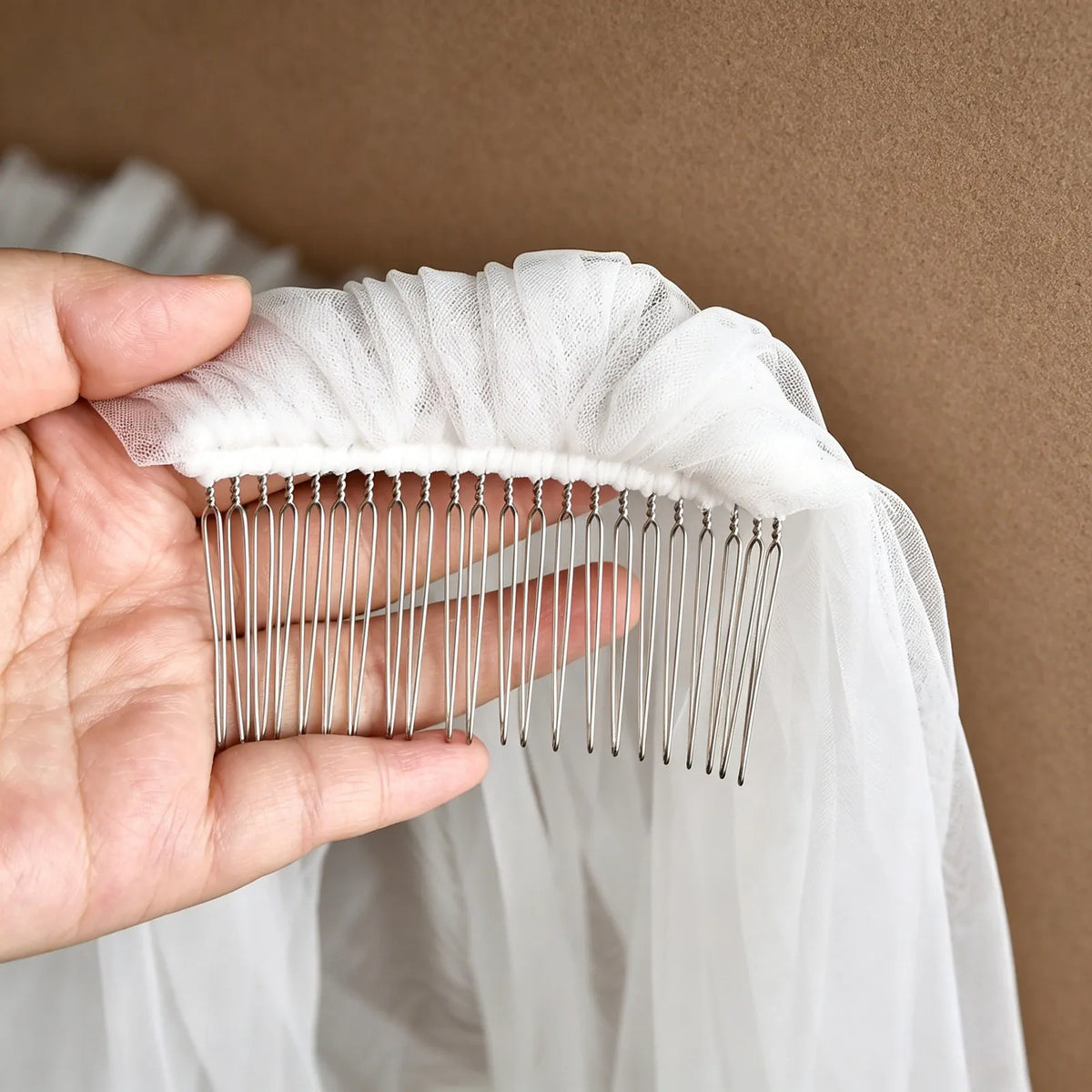 Hand holding pre-attached silver metal hair comb stitched tightly into the soft tulle headpiece