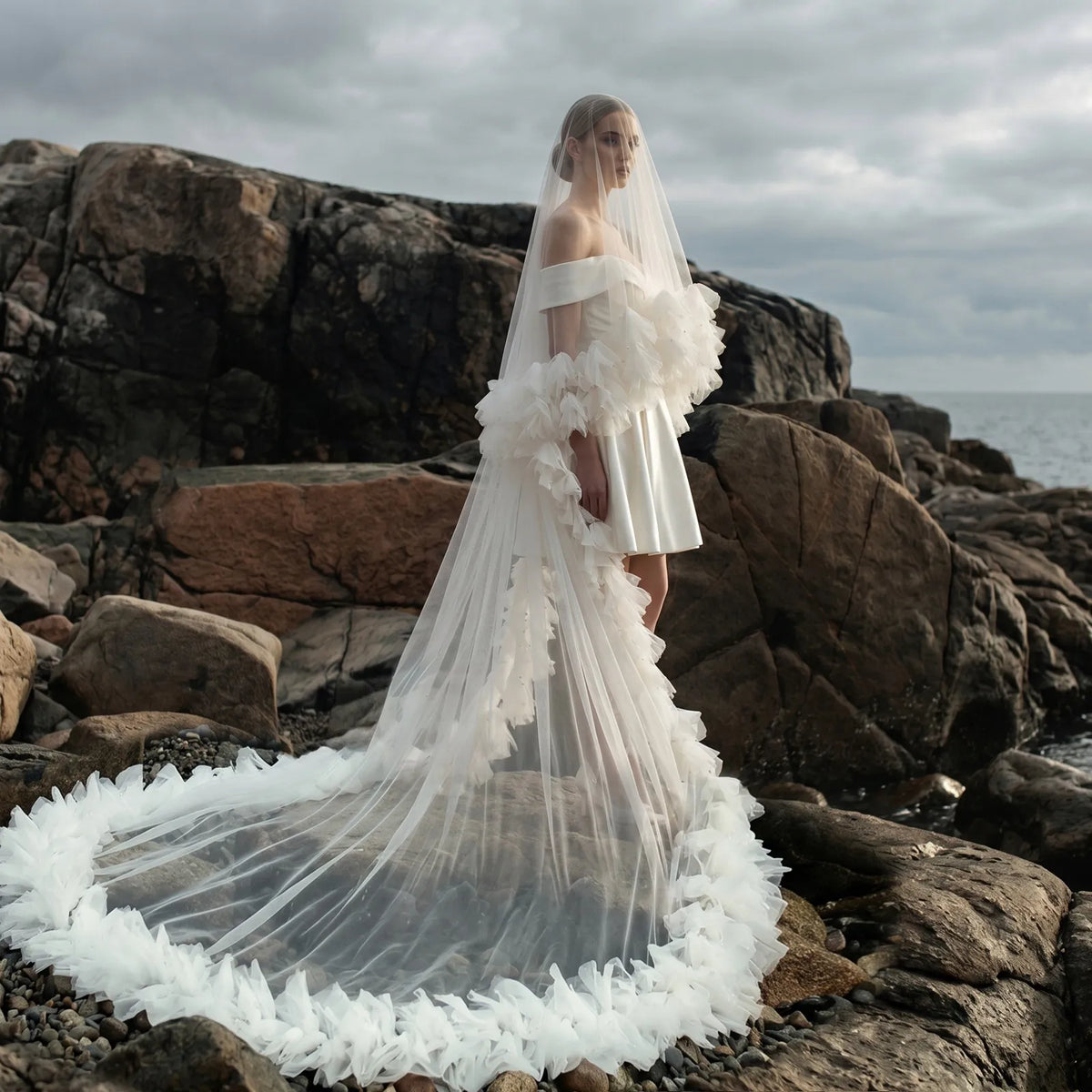 Bride in short dress on rocky coast with sweeping 300cm tulle ruffle train flowing behind