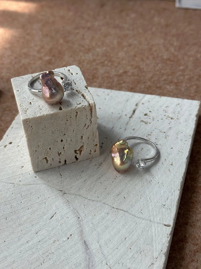 Two bean baroque pearl cubic zirconia open rings with iridescent purple and gold lusters on stone block.