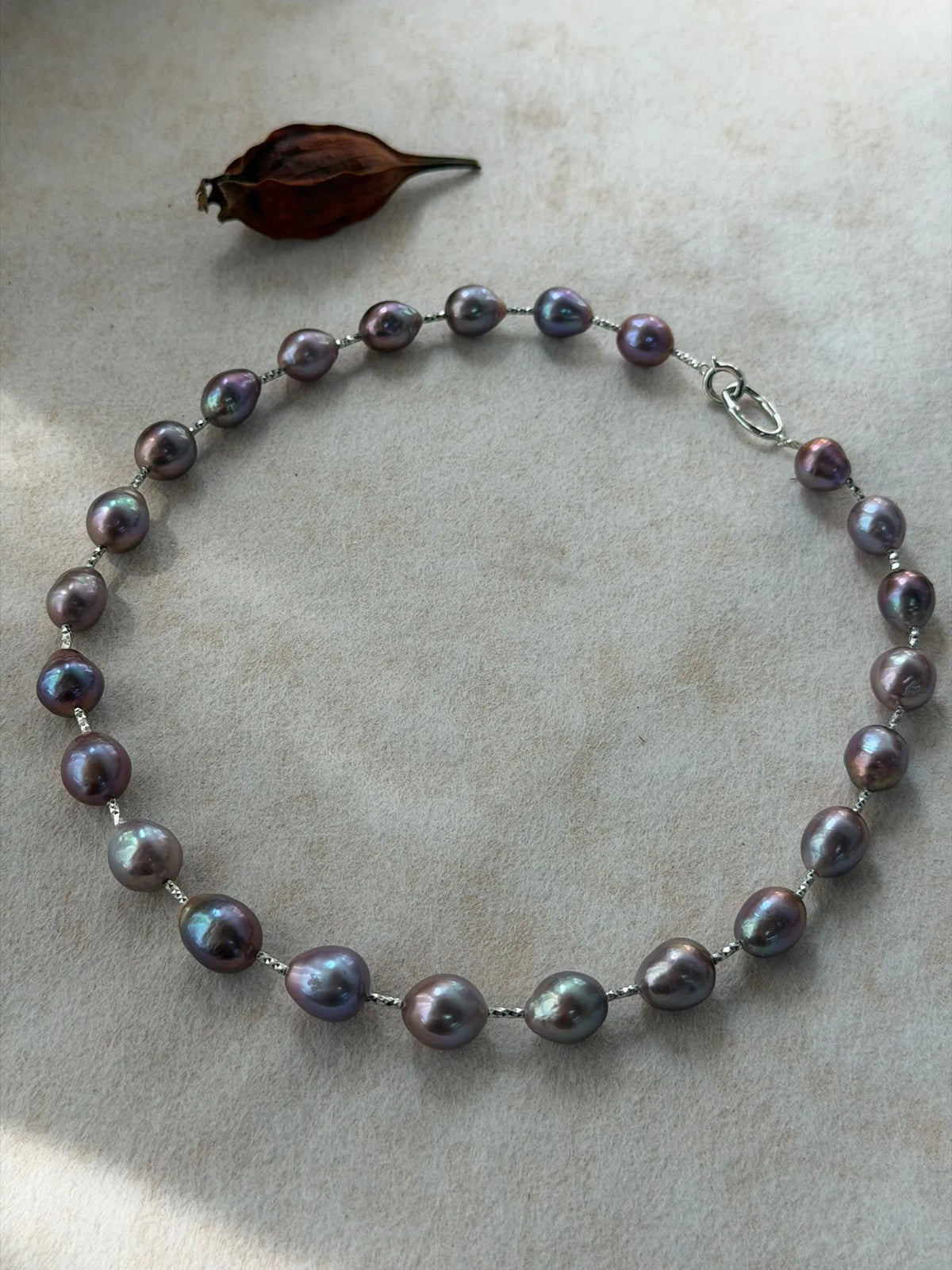 Circular arrangement of deep violet-blue baroque pearl choker necklace with silver hardware.