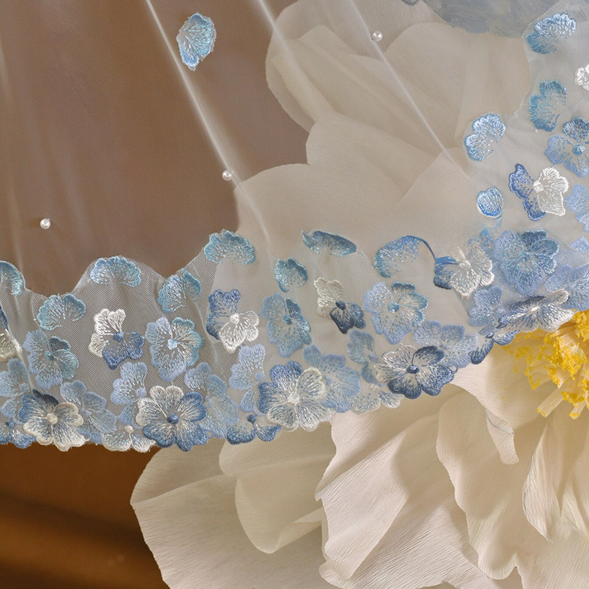 Whimsical romantic single-tier fingertip length bridal veil adorned with blue 3D embroidered floral lace along the edge and scattered lustrous pearl seed accents.