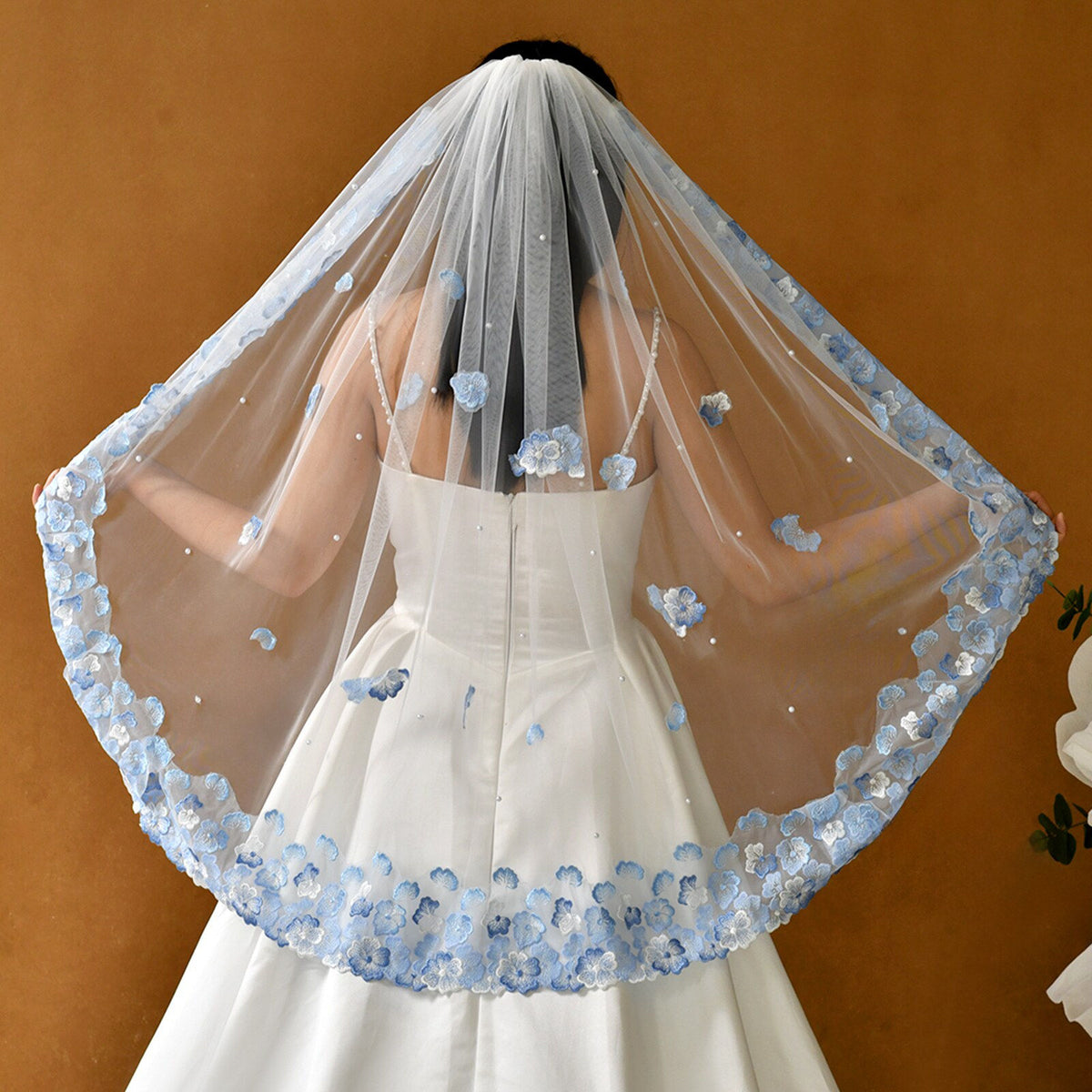 Whimsical romantic single-tier fingertip length bridal veil adorned with blue 3D embroidered floral lace along the edge and scattered lustrous pearl seed accents.