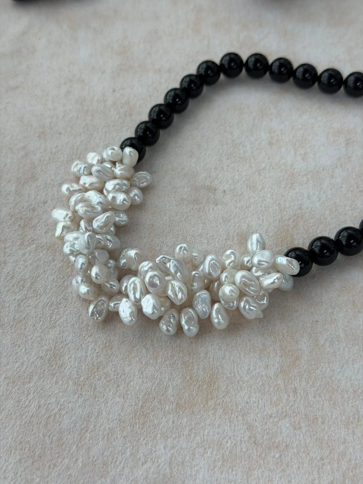 Close-up details of the woven white baroque pearl cluster petals integrated into glossy black onyx beads.